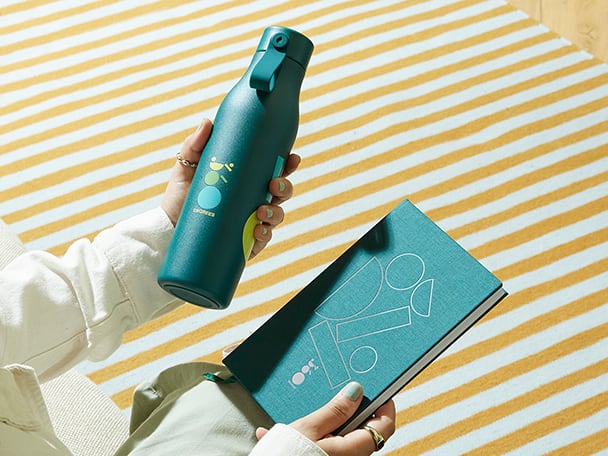 Two hands holding a branded Water Bottle and Notebook 