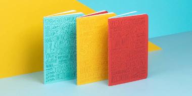 3 Aries Moross notebooks including 1 red, 1 blue and 1 yellow journals with signature Aries Moross typography designs