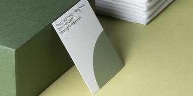 Vertikal strukturierte Visitenkarte mit minimalistischen weißen und grünen Entwurf neben 100% Recycling-Logo auf grünem Hintergrund