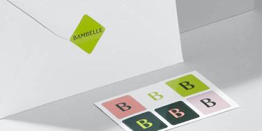 Weißer Umschlag, der durch einen grünen quadratischen Aufkleber und ein Aufkleberblatt von 6 Mini-Logoaufklebern geschlossen wird