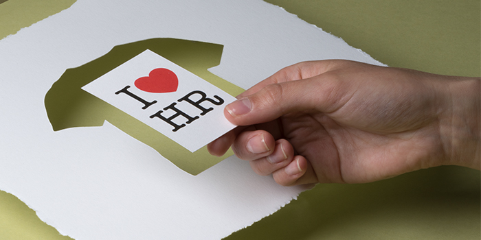 Hand taking a recycled business cards saying I love HR from a sheet of recycled cotton paperwith a t-shirt shaped cutout