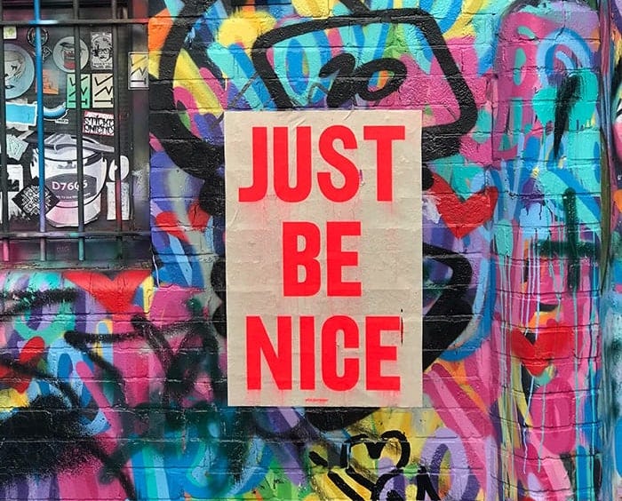 Just be nice poster on a wall covered in graffiti in London