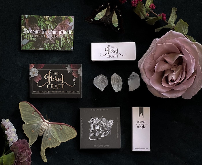 Standard business cards with floral designs, white minicards, square black business cards with a skull design, rose, butterflies and crystals on a black table
