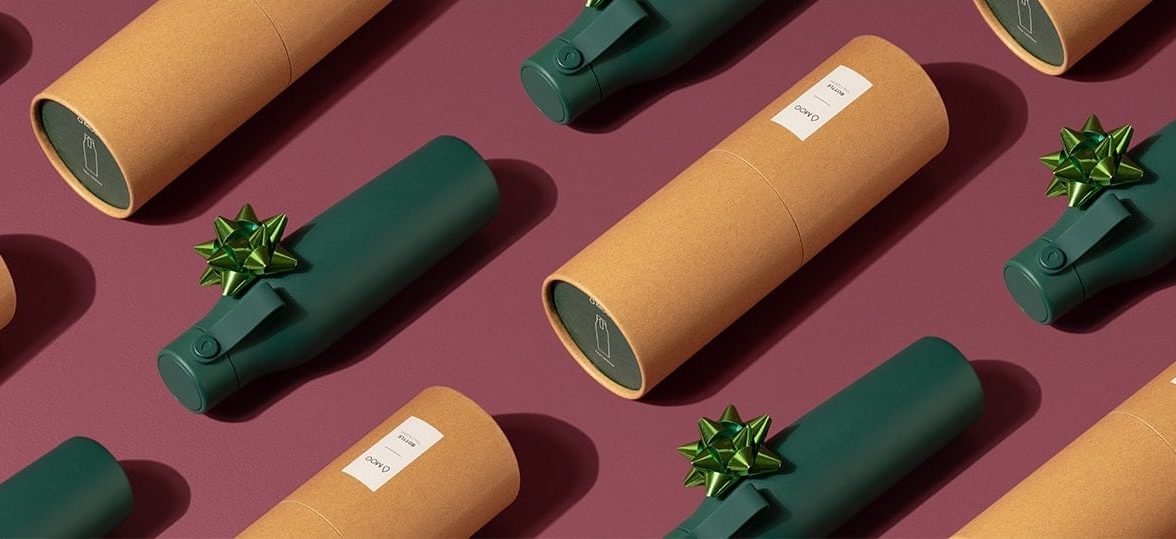 Dark green drink bottles with light green gift bows and their cardboard tube packaging laid out in lines