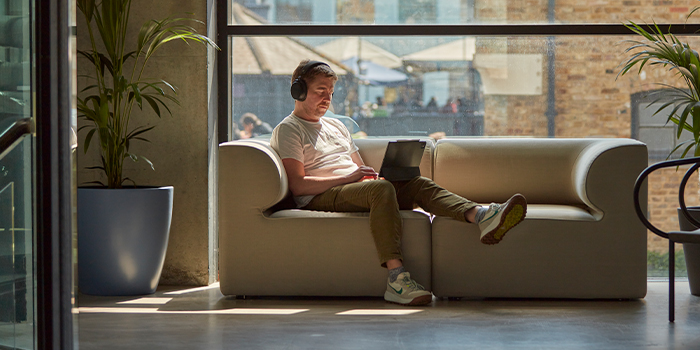 Employee working on sofa, wearing headphones.