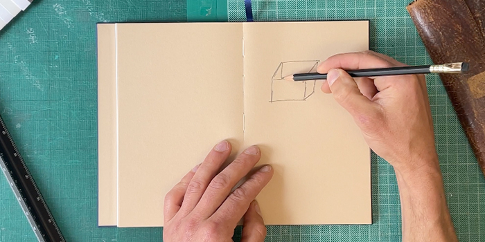 Hands drawing a box in an open notebook with colored pages