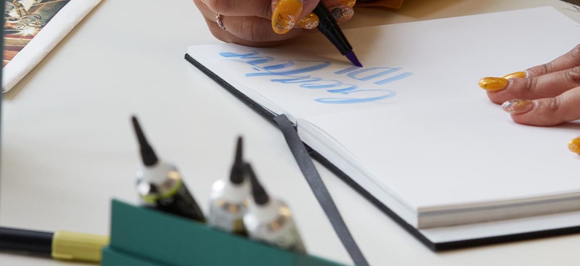 Someone with painted nails doing calligraphy in a notebook