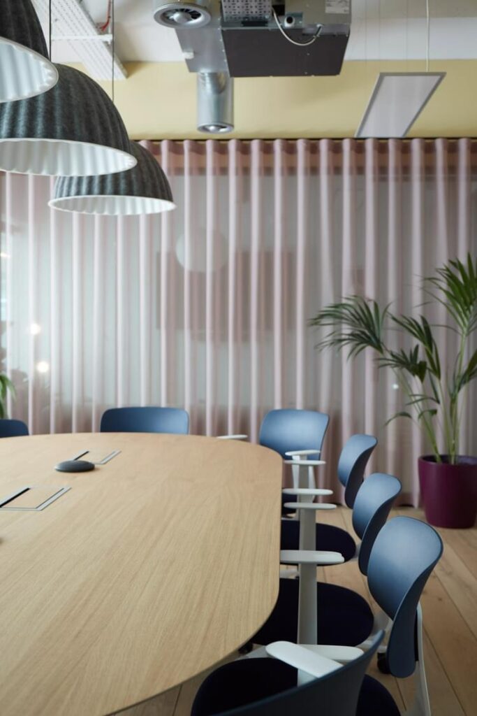 Meeting room with large wooden table, ergonomic chairs, sound absorbing lamp shades and curtains. 