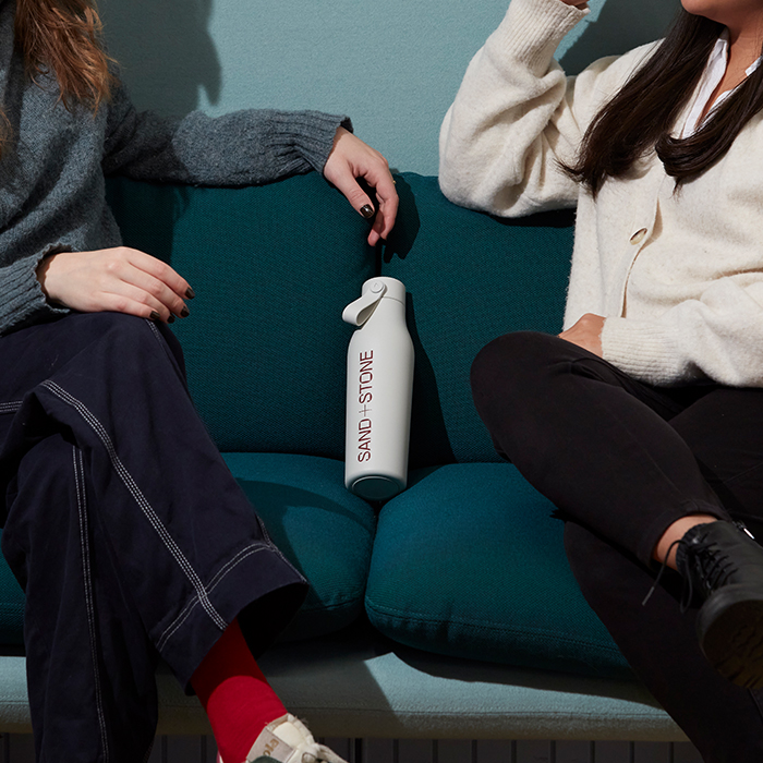 Two MOOsters chatting on sofa with a branded water bottle. 