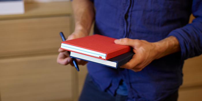 Employee holding two MOO Notebooks and a pen.