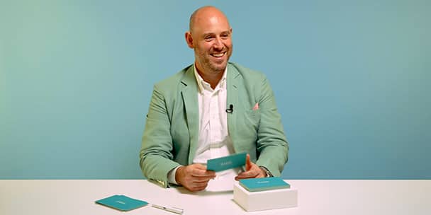Portrait of MOO CEO Richard Moross holding question cards on a blue background