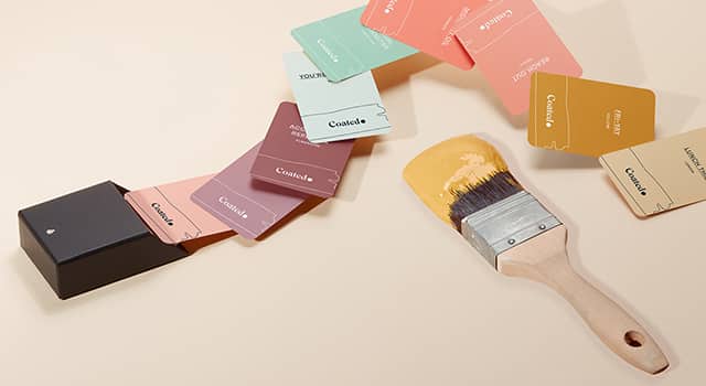 Pincel junto a una colección de coloridas tarjetas de visita dispuestas como un abanico de colores, cada tarjeta en un color diferente y con un mensaje diferente gracias a Printfinity
