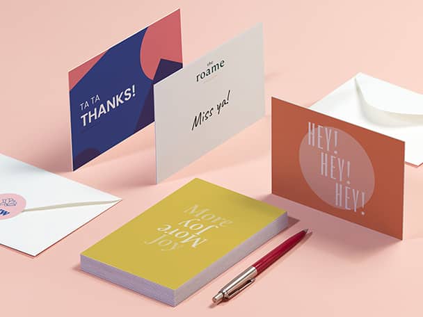 Stationery products including a white envelope with round sticker, 4 different postcard designs, a pen and an envelope