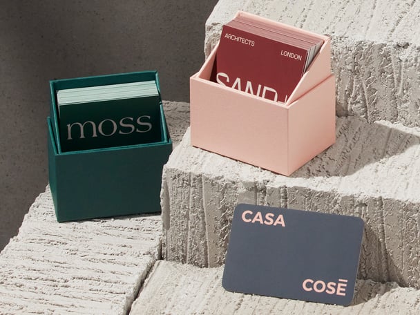 Dos cajas expositoras en verde alpino y rosa pastel sobre fondo de arenisca para tarjetas de visita