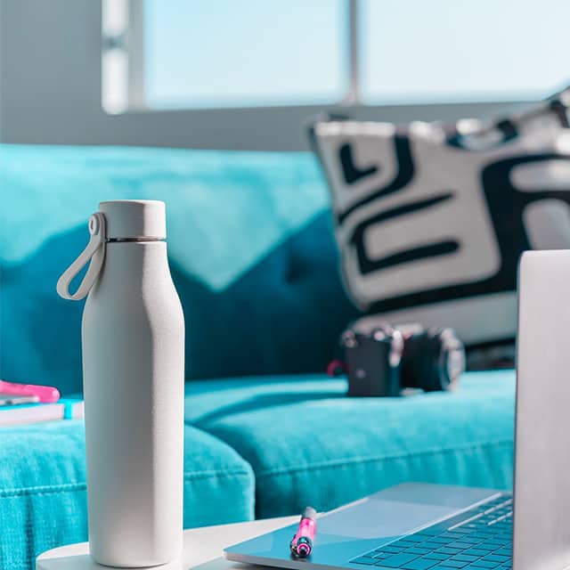 Grey MOO drink bottle on a coffee table next to a blue couch