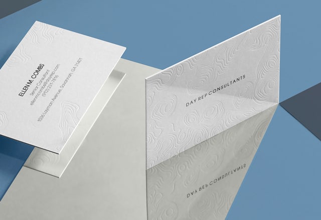 2 Cartes de Visite Letterpress blanches minimalistes avec un design gaufré abstrait rappelant une carte du monde sur un miroir et un fond bleu et gris