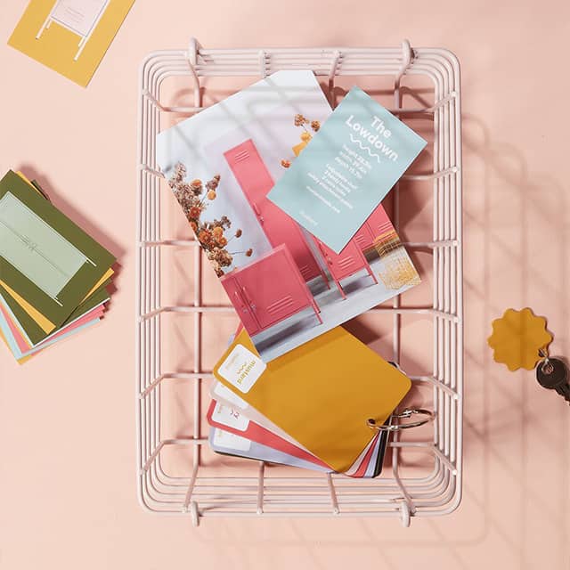 Weißer Drahtkorb mit senffarbenen Farbmustern, Visitenkarten und Produktinfo-Postkarten