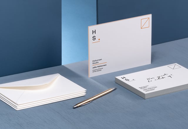 Minimalist, extra-thick note card with a colorful seam next to a pile of luxe note cards, a pen and premium white envelopes