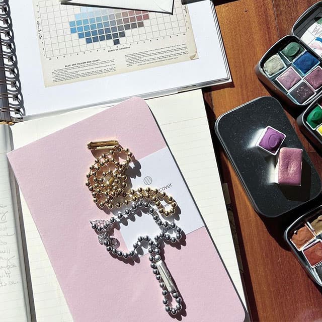 Journal rose à couverture souple posé à plat sur le bureau avec des pots de peinture et du matériel d'art.