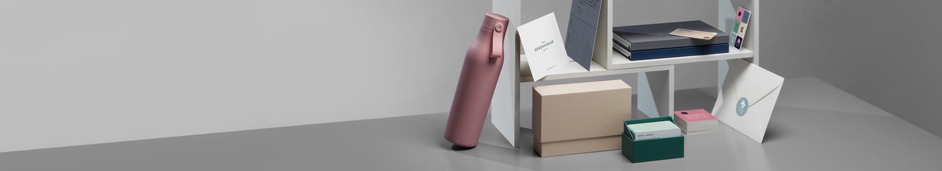 Pink water bottle and white shelf with presentation boxes and stationery including business cards, postcards and notebooks