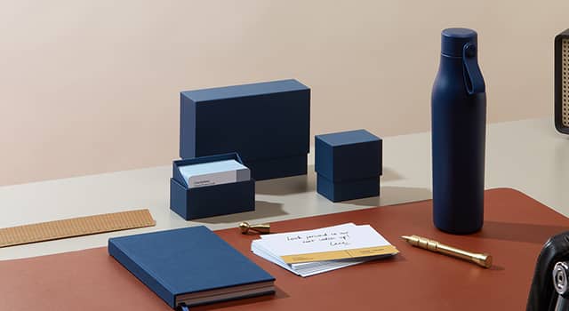 Desk with a blue cloth cover notebook, a blue reusable water bottle, and matching blue display boxes in three sizes to store square cards, business cards and note cards