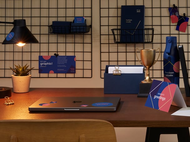 Una scrivania con biglietti d\'auguri, un espositore con cartoline, una borraccia personalizzata e un computer portatile con adesivi.
