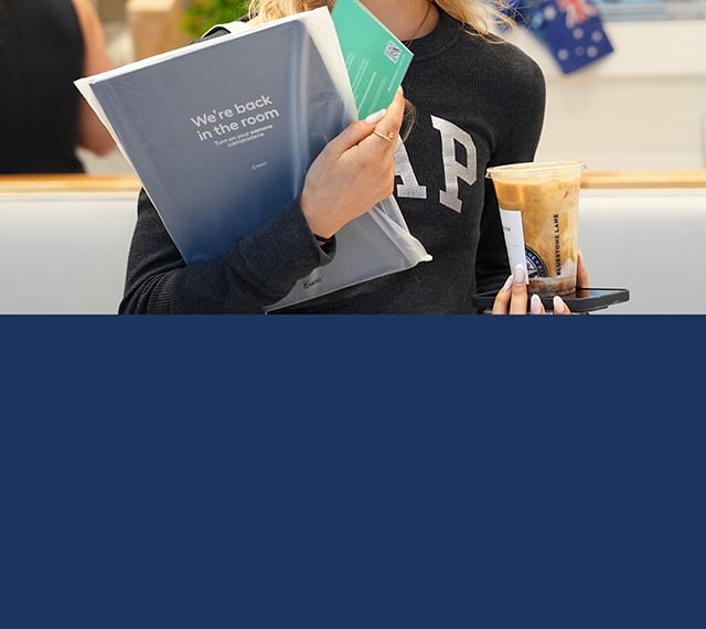 Woman on the go with print materials, phone, and iced coffee on both hands