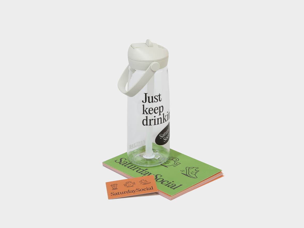 A clear water bottle with a light grey lid, featuring "Just keep drinking" and "Saturday Social" text.