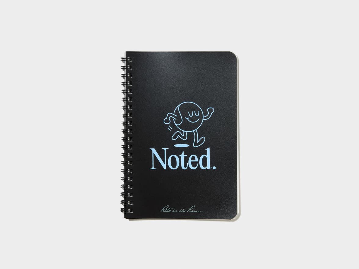 Black spiral-bound notebook with a cartoon character and the text "Noted." and "Rite in the Rain" in light blue.