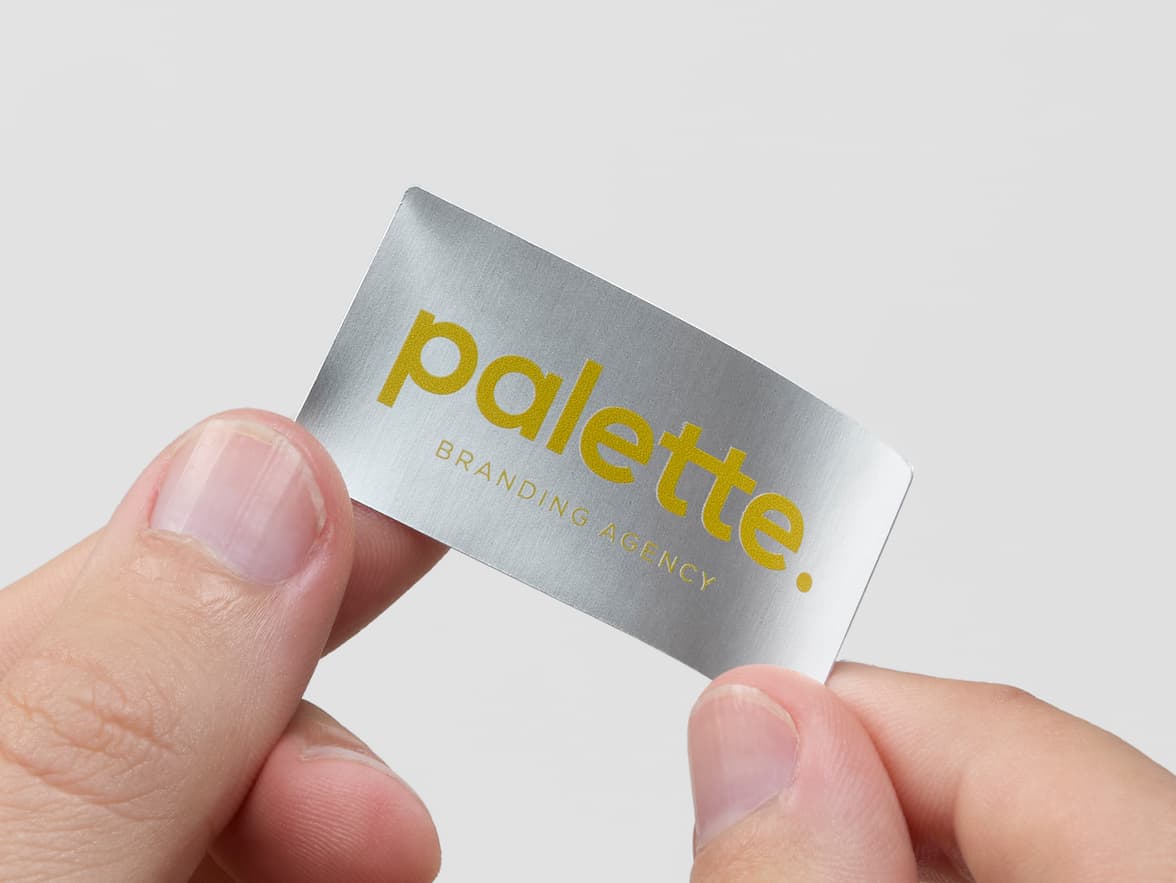 Hands holding a silver rectangular metallic sticker with yellow branding.