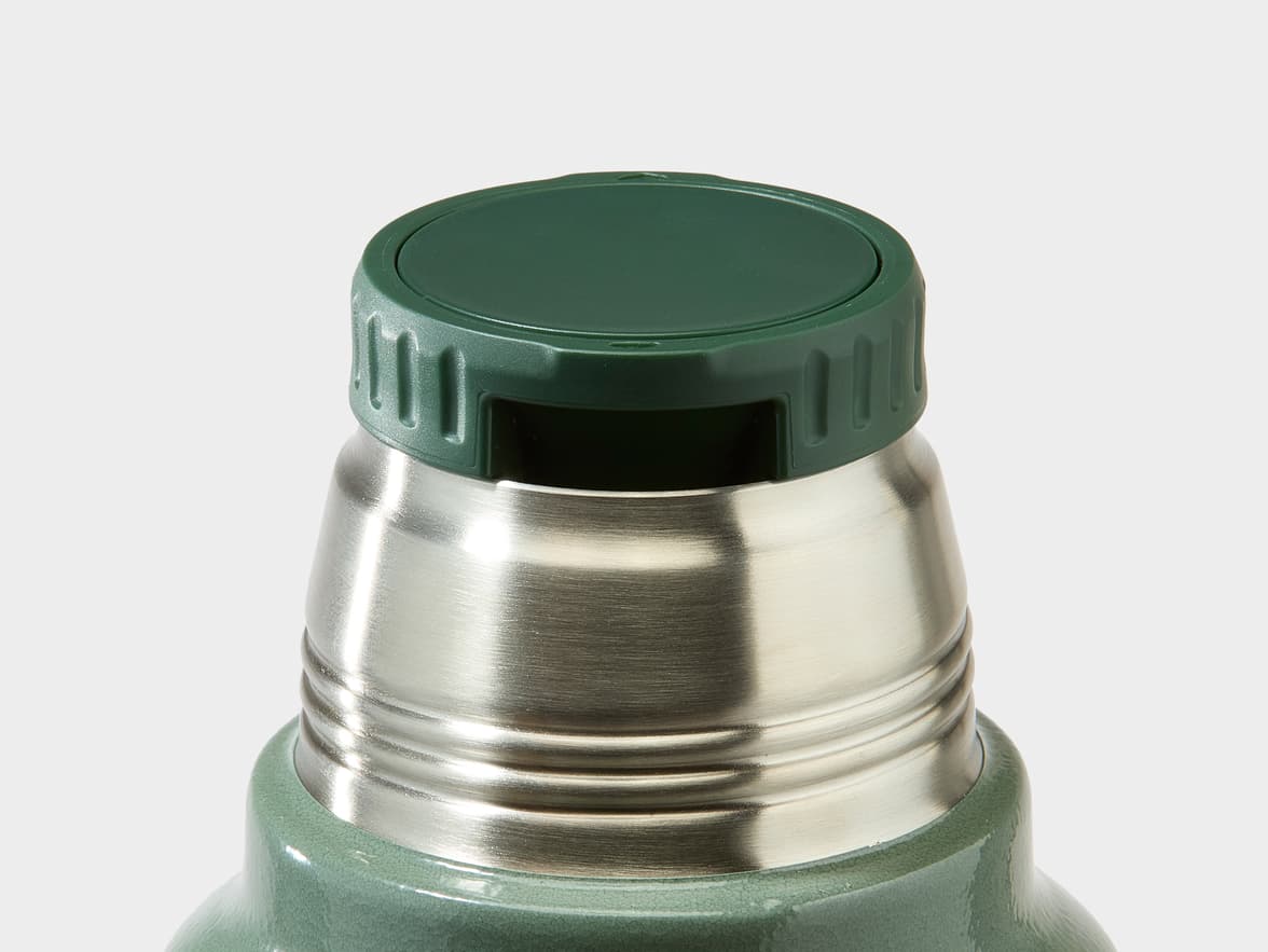 Close-up of a Stanley thermos, showing its dark green plastic cap and brushed stainless steel top.