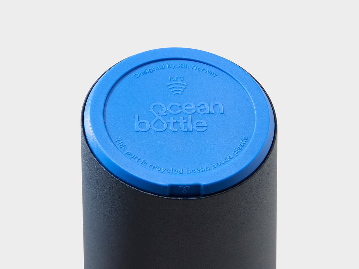 Blue lid of an Ocean Bottle showing the 'Ocean Bottle' logo, 'NFC' symbol, and text: 'Designed by K8, Norway' and 'This part is recycled ocean bound plastic'.