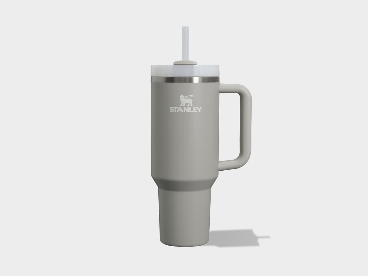 A grey Stanley travel mug with a handle and straw, casting a shadow on a light background.
