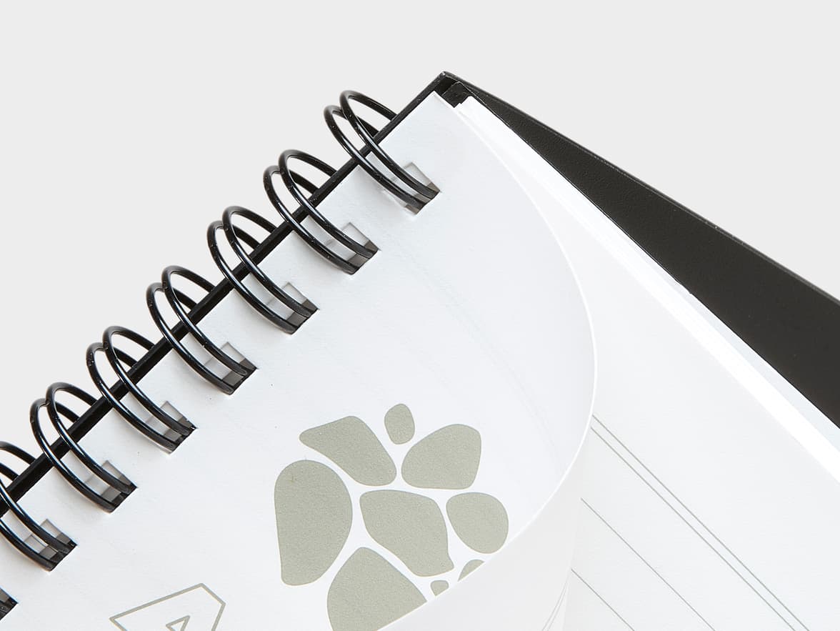 A black spiral-bound notebook with white pages and a grey abstract pattern.