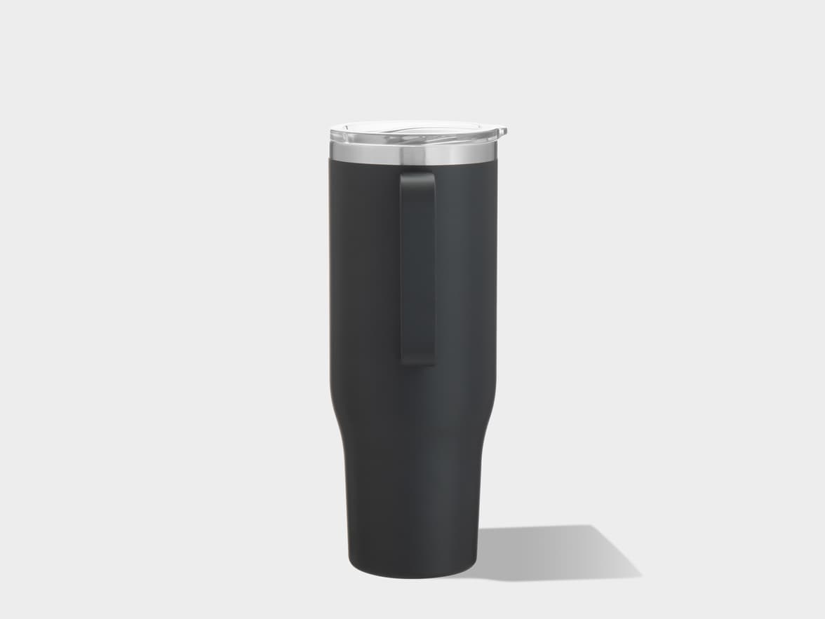 A tall, matte black insulated tumbler stands upright on a plain light gray surface. The tumbler has a wide mouth with a clear, transparent plastic lid featuring a small sip opening. Below the lid, there is a prominent shiny silver band. An integrated, vertical handle extends down one side of the tumbler. Soft, even lighting illuminates the object, casting a subtle, dark shadow to its right on the surface.
