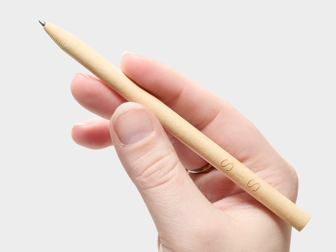 A hand holds a light-colored pen with 'S X S' carved on its side.