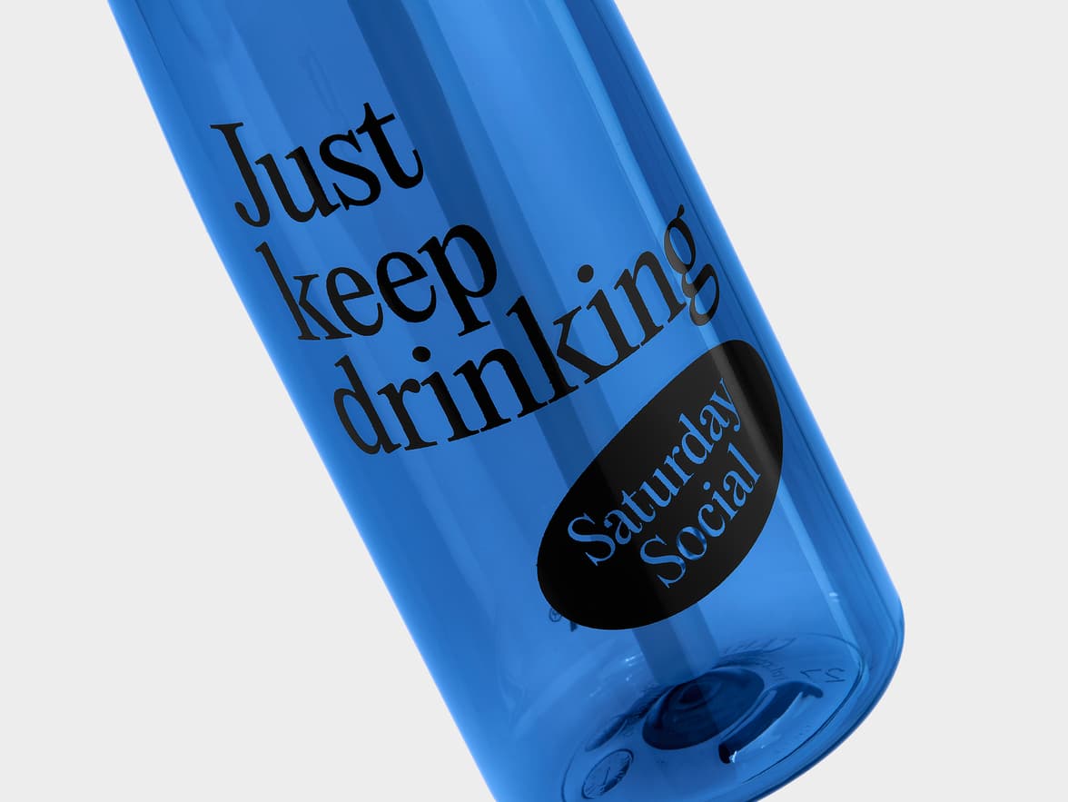 Blue water bottle with the text "Just keep drinking" and branding "Saturday Social".
