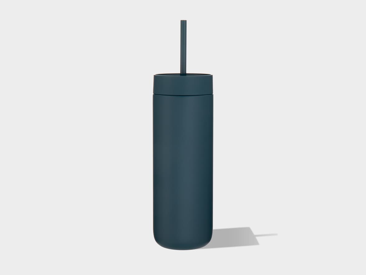 A dark blue, matte tumbler with a matching straw protruding from its lid stands upright on a light grey background, casting a soft shadow to its right.