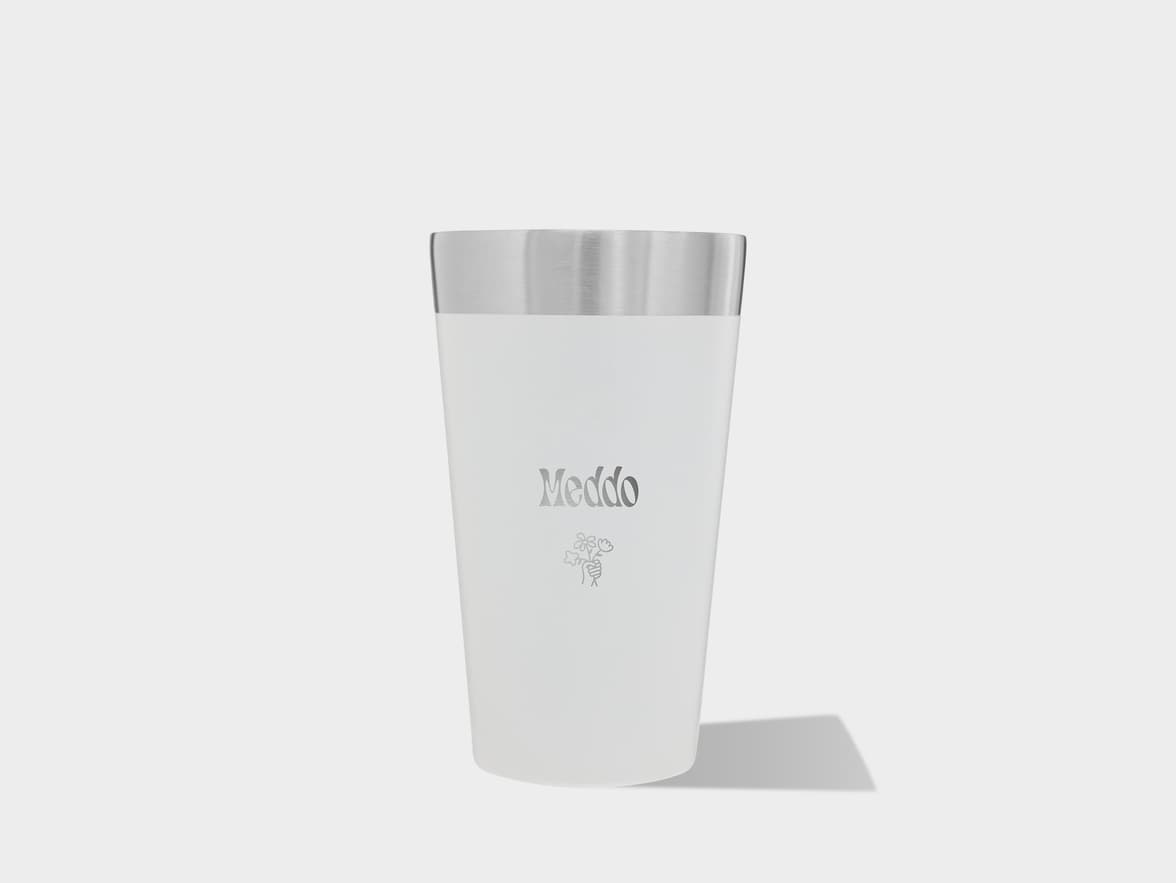 A white tumbler with a metallic top, "Meddo" text, and a floral graphic, casting a shadow on a light gray background.