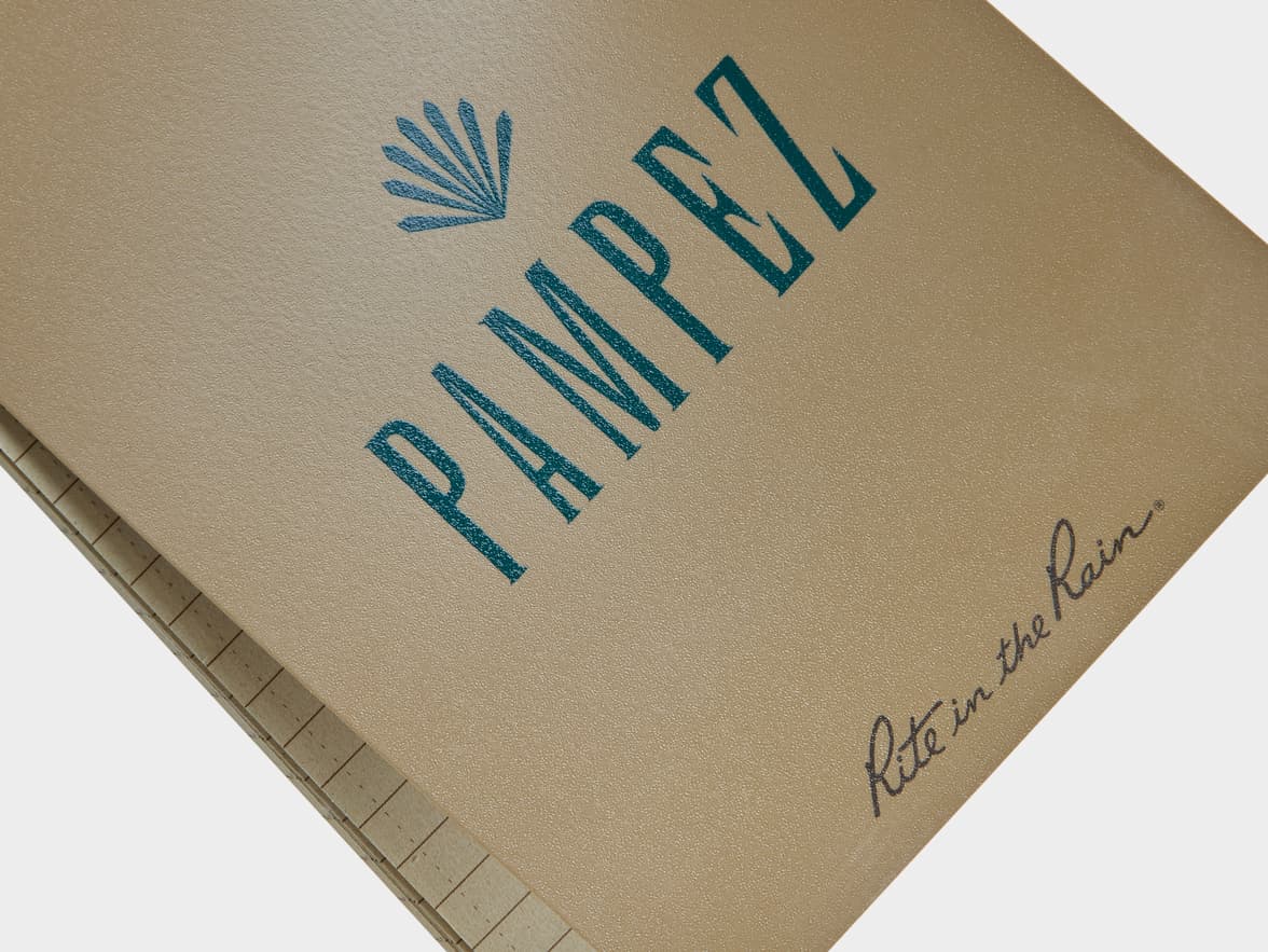 A brown notebook with "PAMPEZ" and a fan logo, and "Rite in the Rain®" printed on the cover.