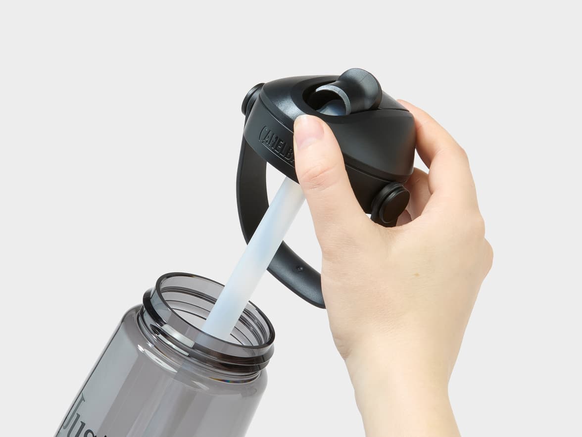 A hand opens a grey CamelBak water bottle with a straw, displaying 'Just' branding.