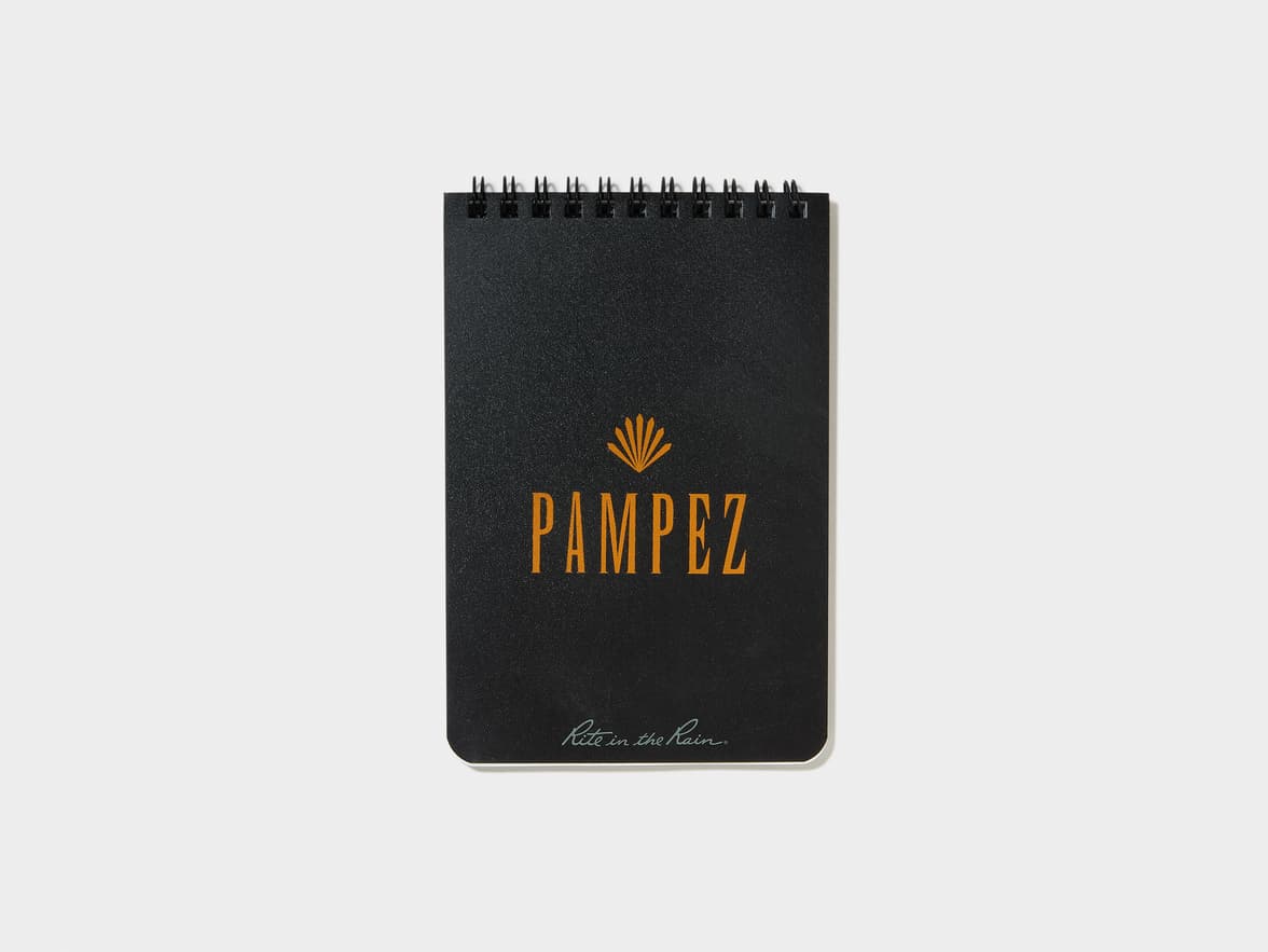 Black spiral-bound notebook with "PAMPEZ" in orange above a fanned symbol, and "Rite in the Rain." in teal at the bottom.