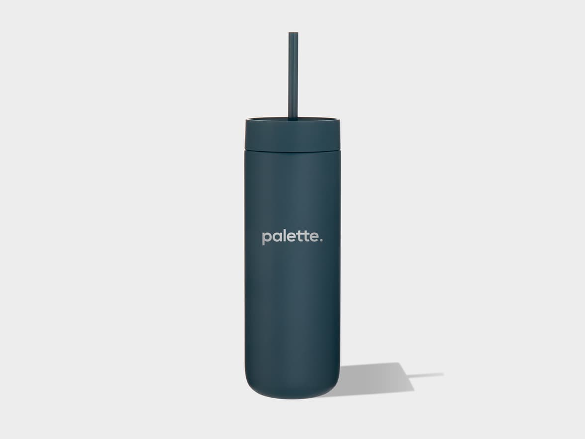 A tall, cylindrical, matte dark teal travel mug with a matching straw stands upright on a light grey background, casting a subtle shadow. The word "palette." is printed in silver lettering on the front of the mug.