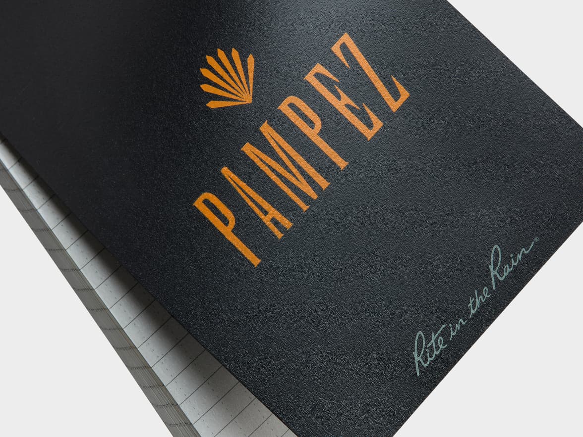 A black notebook with "PAMPEZ" and a fan logo in orange, and "Rite in the Rain®" in light blue script on the cover.