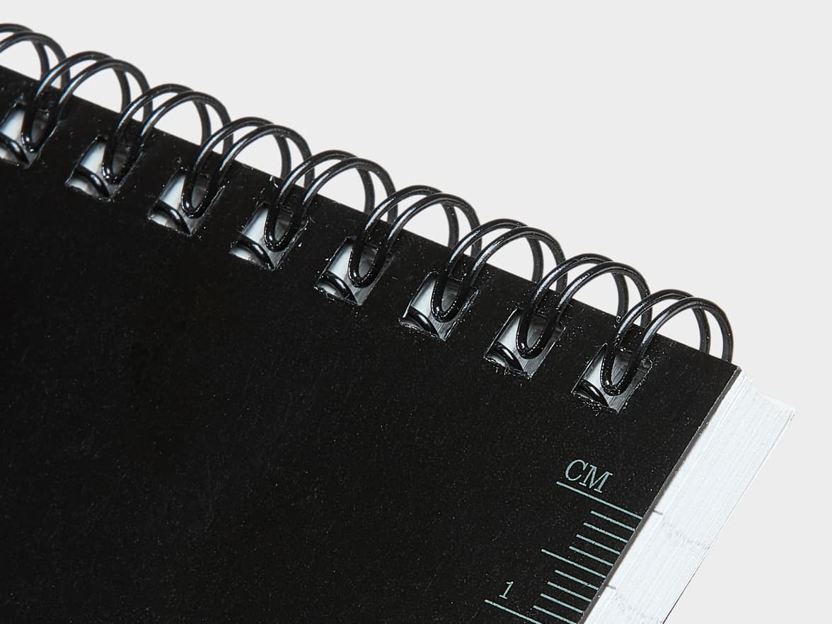 A black spiral-bound notebook with "CM" and a ruler scale printed on its cover.