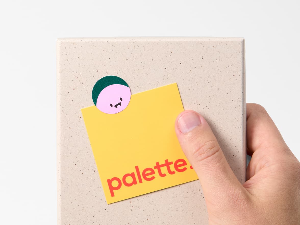 A hand holding a box with a square piece of paper stuck to it with a round coated sticker.