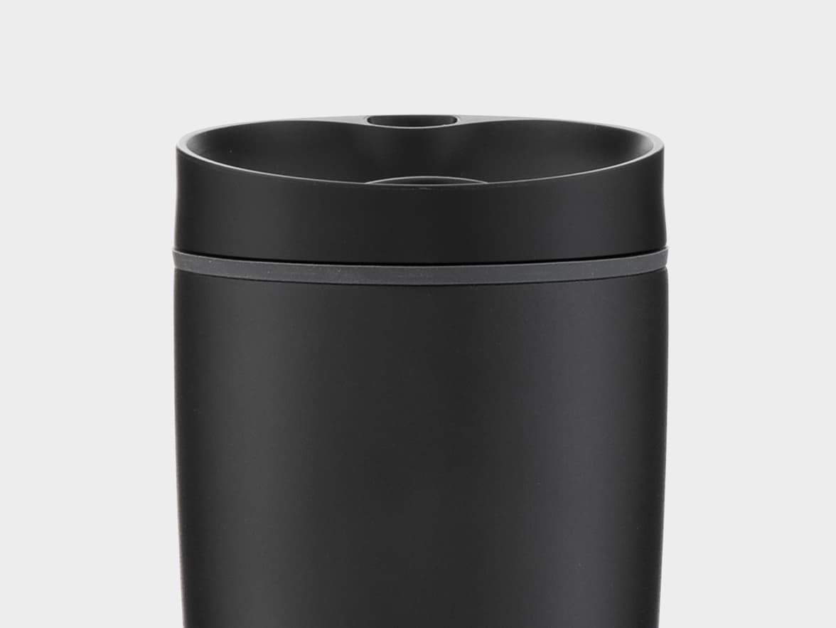 A close-up of the top section of a black matte travel mug, showing a grey band below the rim and a contoured opening at the top.