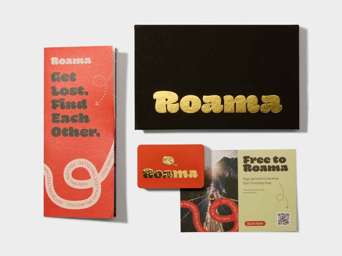 Roama brand collateral: a red booklet, black box with gold logo, orange card, and a yellow flyer, on a white background.