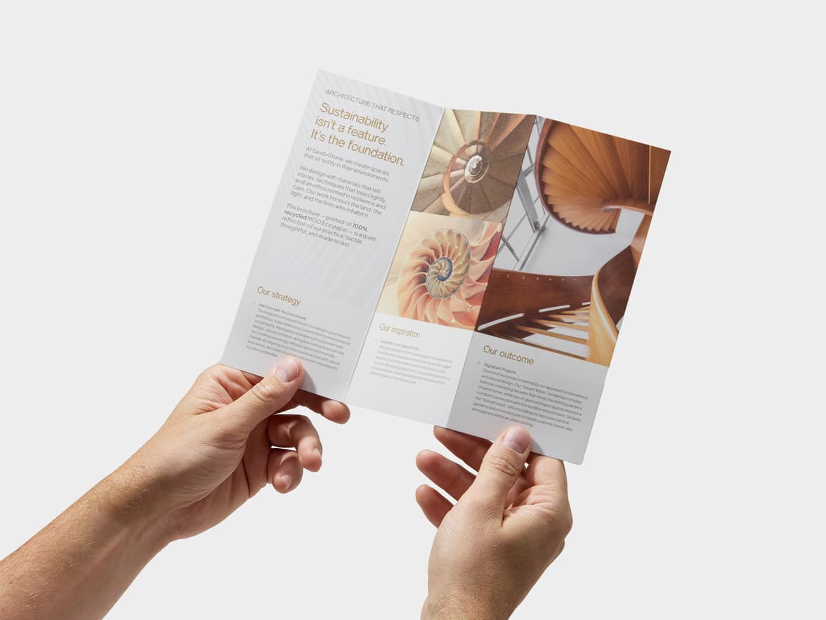 Two hands hold an open z-fold brochure displaying text about sustainable architecture and images of natural spiral patterns.