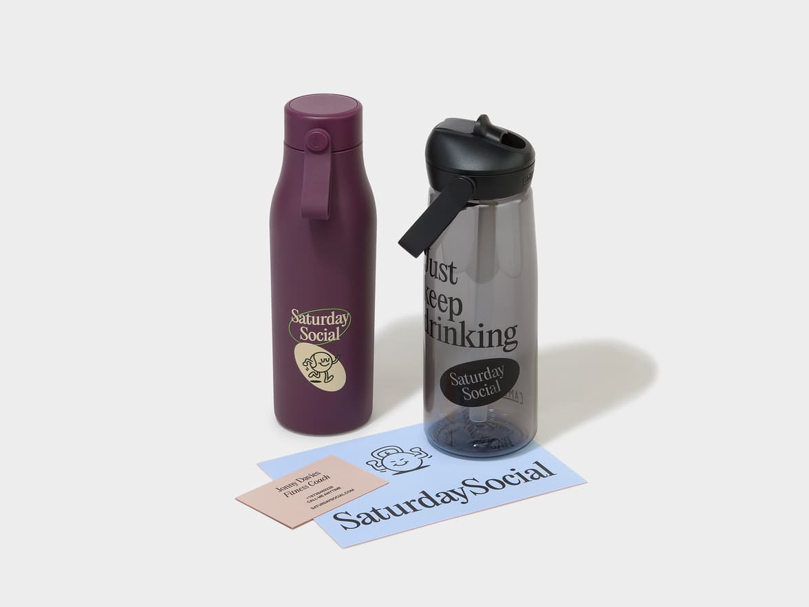 A purple water bottle with "Saturday Social" branding and a character logo, alongside a clear water bottle featuring "Just keep drinking" and "Saturday Social" text.